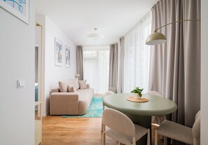 A modern living room with a sofa, a dining table with chairs, a hanging lamp, and a large window with curtains. - Browary Warszawskie Superior Apartment (Warszawa)