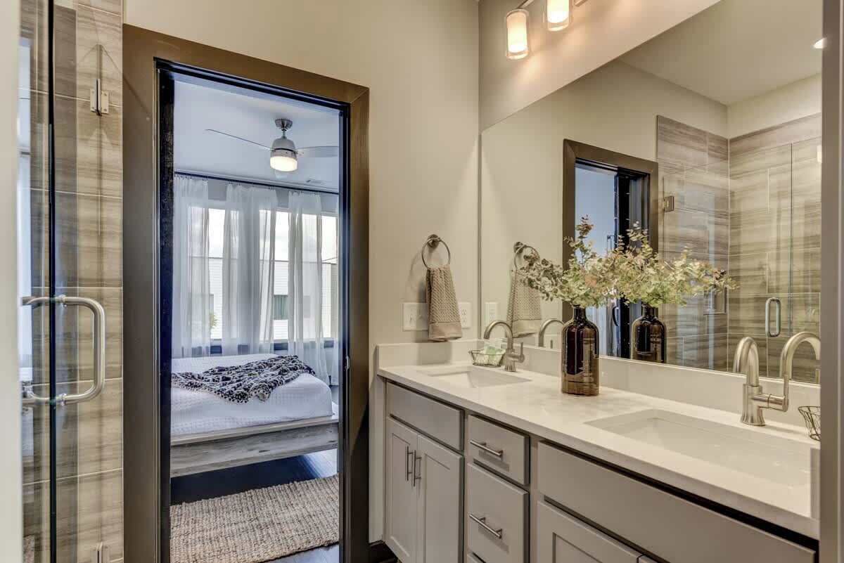 Un baño moderno con un espejo grande, lavamanos dobles y vistas hacia un dormitorio.