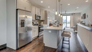 Une cuisine moderne dotée d’appareils électroménagers en acier inoxydable, d’un îlot central, de luminaires suspendus et offrant une vue sur l’extérieur.