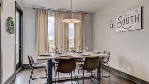 Un coin repas avec une table dressée pour quatre personnes, un luminaire suspendu et un panneau fixé au mur.