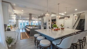 A modern kitchen with a large island, bar stools, and pendant lighting. - Luxury Meets the Beach! Private Pool/Hot Tub/Linens/11BR/Parking Steps to Beach! (Dewey Beach)
