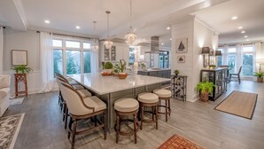 A spacious kitchen with a large island, bar stools, pendant lighting, and a view of the outdoors. - Luxury Meets the Beach! Private Pool/Hot Tub/Linens/11BR/Parking Steps to Beach! (Dewey Beach)