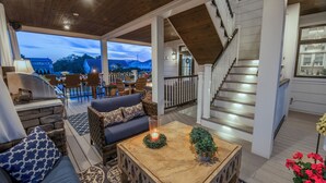 A cozy living area with a stone fireplace, a sofa, and a coffee table. There is a staircase with a railing and a view of the outside. - Luxury Meets the Beach! Private Pool/Hot Tub/Linens/11BR/Parking Steps to Beach! (Dewey Beach)