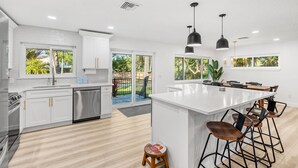 A modern kitchen with white cabinetry, a large island with bar stools, and a view of the backyard.