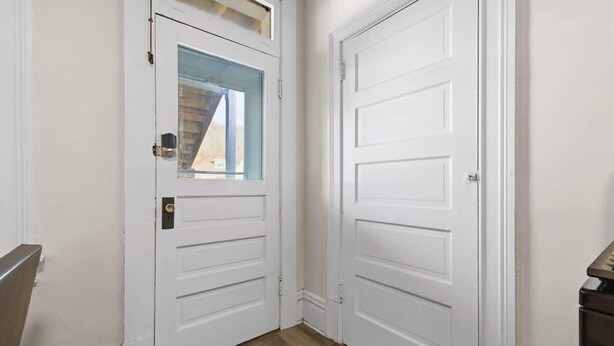 Una puerta blanca con ventanal, suelo de madera y baranda de metal.