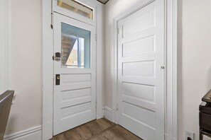 Une porte blanche avec une fenêtre, un plancher en bois et une rambarde en métal.