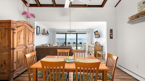 A dining area with a wooden table and chairs, a ceiling fan, and a view of the sea through a glass door. - Unique Bayfront Townhome with a Prime Location (Ocean City)