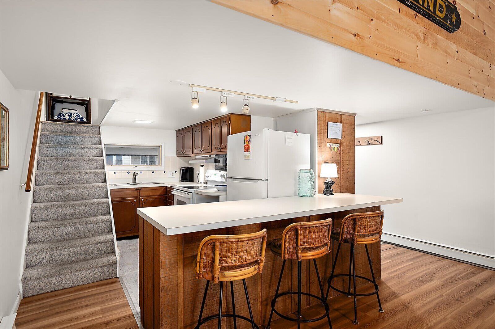 A modern kitchen with a central island, bar stools, wooden cabinets, and a staircase leading to another level.