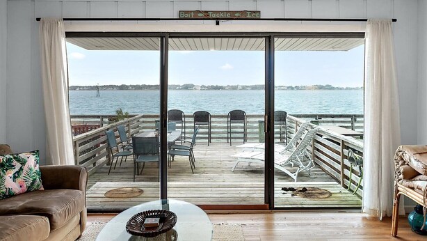 A room with a large sliding glass door leading to a deck with outdoor seating and a view of the water. - Unique Bayfront Townhome with a Prime Location (Ocean City)
