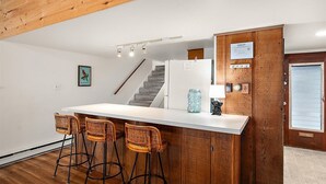 A kitchen with a central island, bar stools, a refrigerator, a staircase, and a wooden door with a sign. - Unique Bayfront Townhome with a Prime Location (Ocean City)