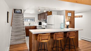 A modern kitchen with a central island, wooden bar stools, and a staircase leading to another level. - Unique Bayfront Townhome with a Prime Location (Ocean City)