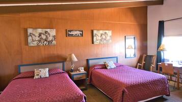 A hotel room with two beds, wooden panel walls, artwork, a desk, and a chair.