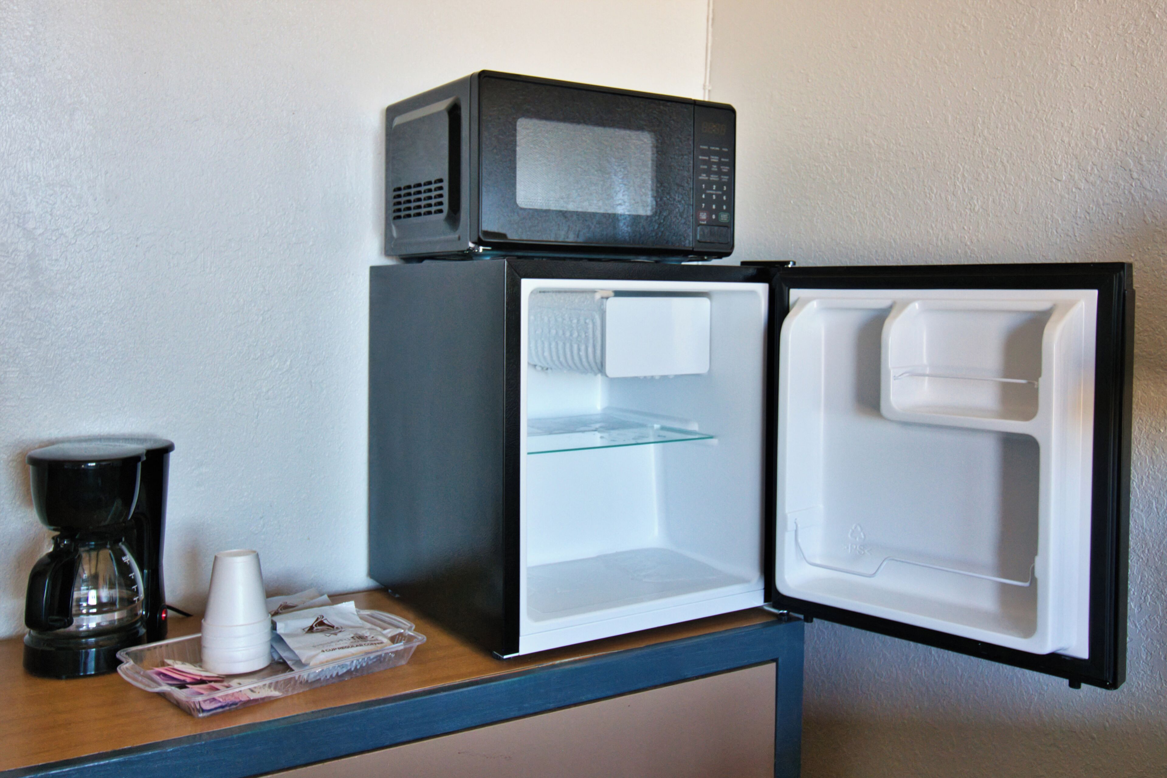 A compact refrigerator with a microwave on top, a coffee maker, and a tray with cups and papers.