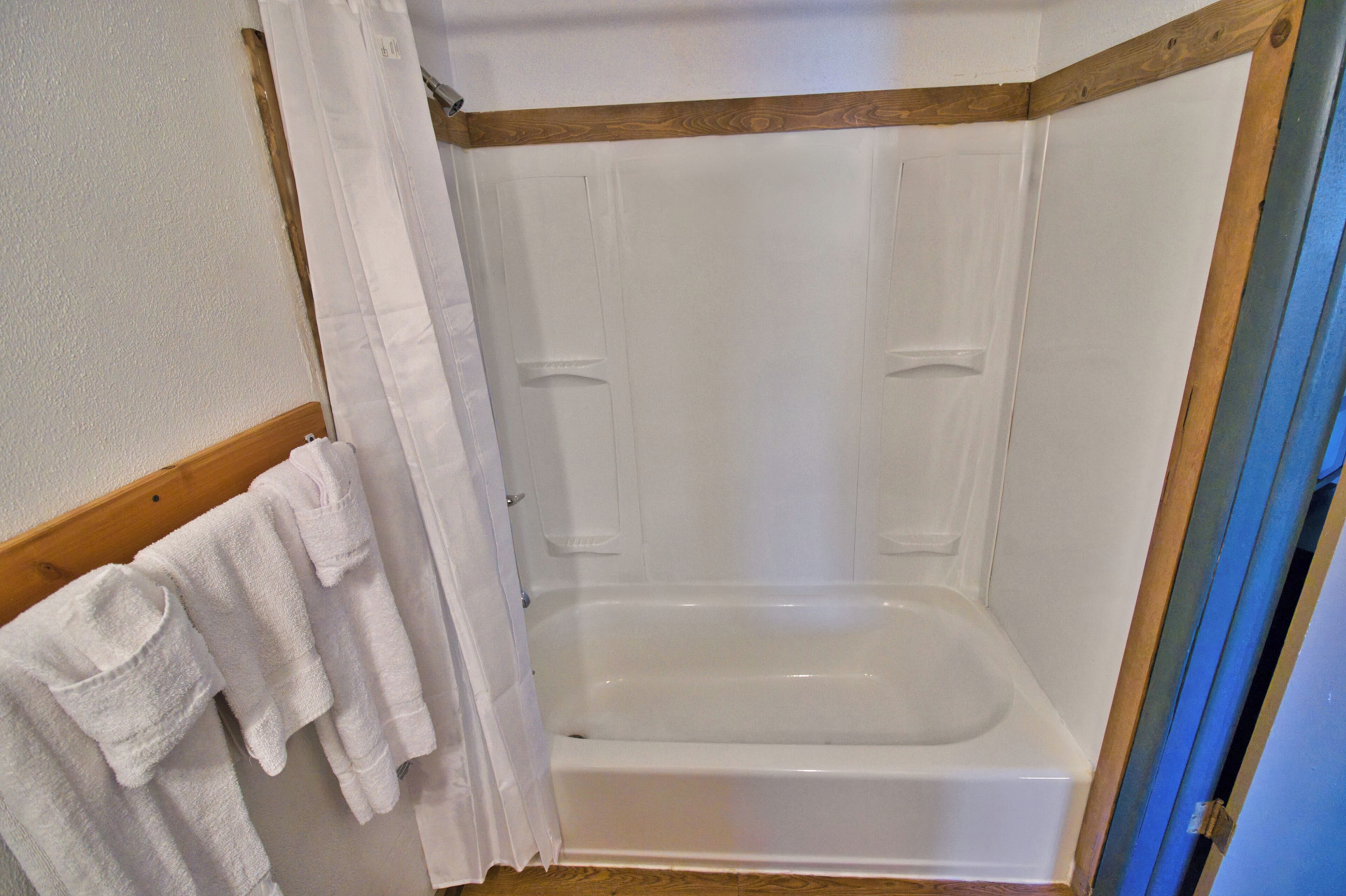 Una ducha con mampara de madera, una bañera blanca y un perchero con toallas.