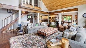 A spacious living area with a high ceiling, a staircase, a sofa set, a coffee table, and a rug. - Gliemwood II at Clam Lake | 5BR Lakefront Retreat (Clam Lake)