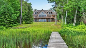 A large house with a deck, surrounded by dense forest and a pond. - Gliemwood II at Clam Lake | 5BR Lakefront Retreat (Clam Lake)