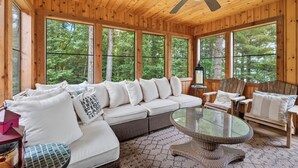 A wooden cabin interior with a sofa, chairs, a glass table, and large windows. - Gliemwood II at Clam Lake | 5BR Lakefront Retreat (Clam Lake)
