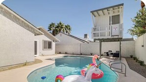 Um quintal com piscina, boias de flamingos e unicórnios infláveis, um espaço coberto de varanda e uma pequena área de estar externa.