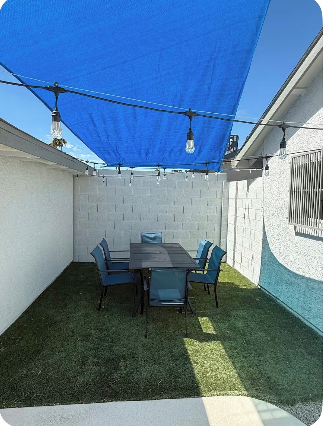 Een terras met een tafel en stoelen, een blauw zonnescherm en lichtslingers.