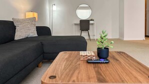 A modern living room with a dark sofa, a wooden coffee table, a small potted plant, and a desk with a chair in the background. - Chic Skokie Retreat - 1BR Unit in Skokie (Skokie)