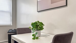 A white table with a potted plant, two chairs, a framed picture on the wall, and a window with blinds. - Chic Skokie Retreat - 1BR Unit in Skokie (Skokie)