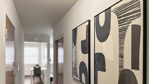 A hallway with two abstract paintings on the wall, a door on the left, and a blurred room in the background. - Chic Skokie Retreat - 1BR Unit in Skokie (Skokie)