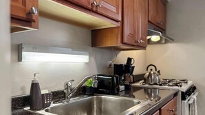A kitchen with a stainless steel sink, granite countertop, wooden cabinets, a coffee maker, and a gas stove. - Chic Skokie Retreat - 1BR Unit in Skokie (Skokie)