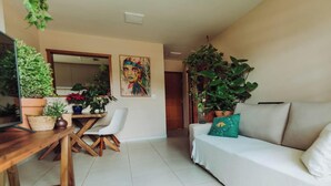 Een woonkamer met een witte bank, een eettafel met stoelen en diverse potplanten.