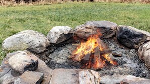A campfire surrounded by rocks in a grassy area.