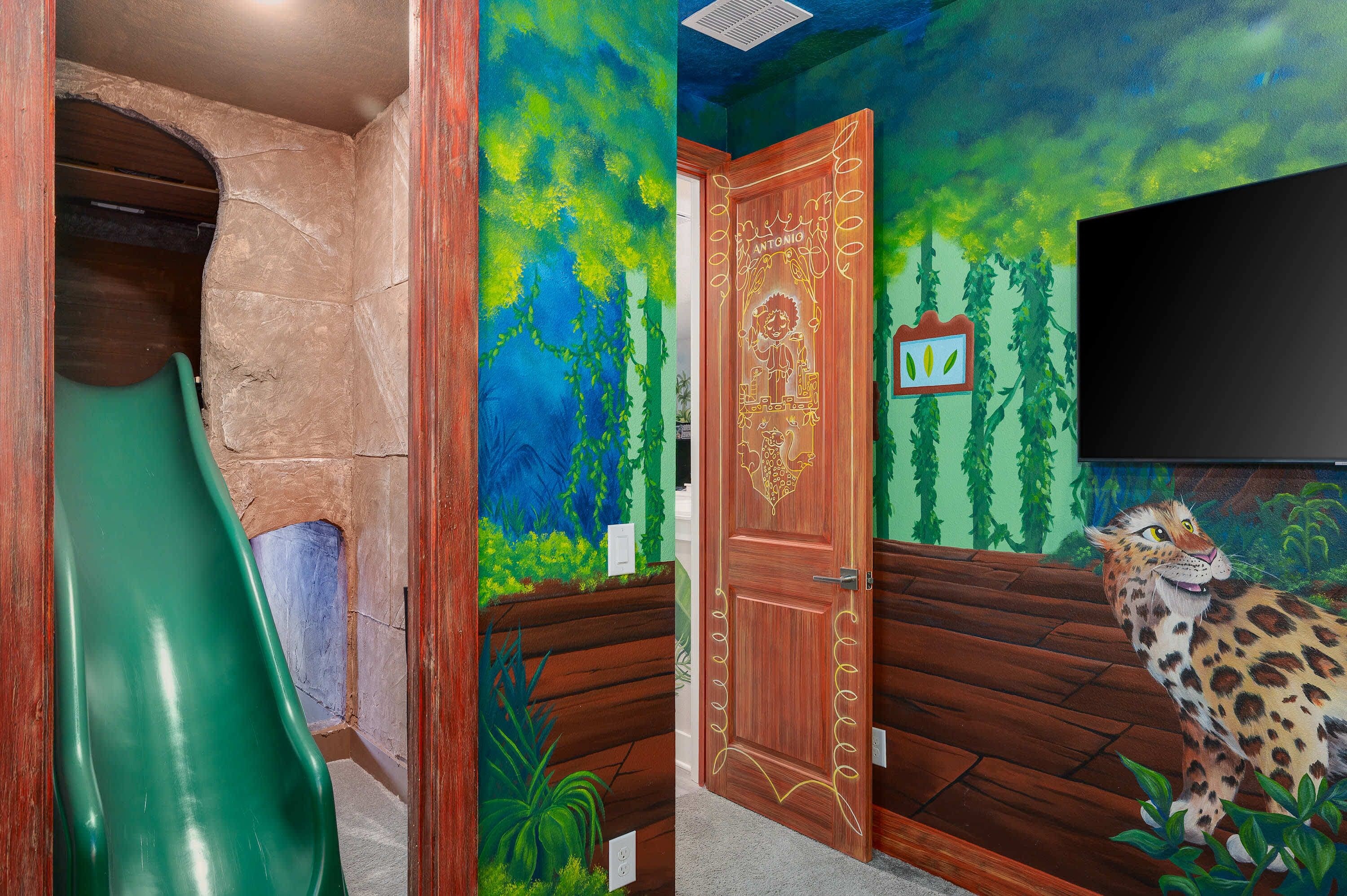 A children's play area with a slide, a door with a forest mural, and a leopard decoration.