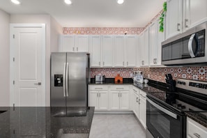 A modern kitchen with white cabinets, a stainless steel refrigerator, a microwave, and a coffee maker. - 6BR Reunion Villa w/ Pool, Cinema & Games (Kissimmee)