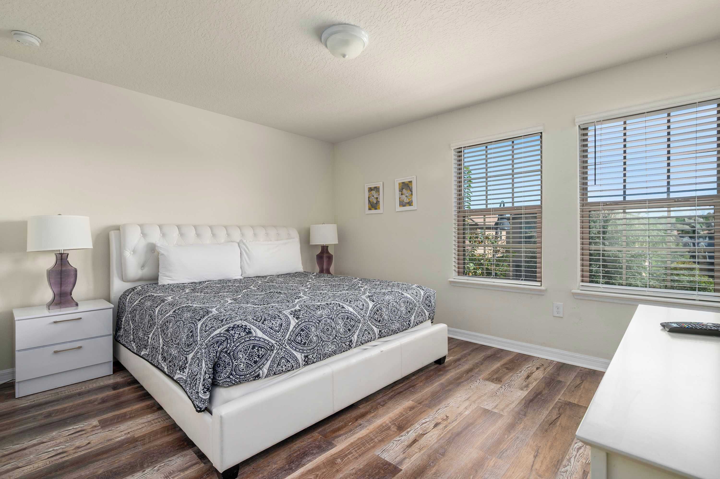 A bedroom with a bed, nightstands, a desk, and windows.