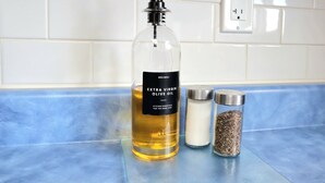 A kitchen counter with a bottle of Extra Virgin Olive Oil, a container of salt, and a container of pepper.