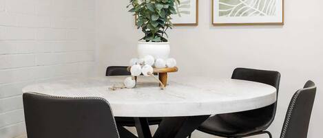 Een eethoek met een ronde tafel, zwarte stoelen en twee bladpatronen in lijsten aan de muur.