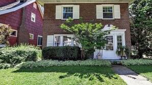 A two-story brick house with a front porch, white shutters, and a small tree in the front yard. - 5 Bedroom Home w/ Private Parking Near Niagara Falls (Niagara Falls)