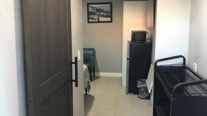 A narrow hallway with a dark wooden door on the left, a teal chair and a small table in the center, and a black metal rack on the right. - Pleasant 1-bedroom NEW Studio 3 with NEW AC in Pinellas Park (Pinellas Park)