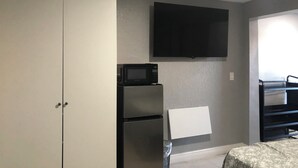 A compact room with a kitchenette, a flat-screen TV mounted on the wall, and a bed with a floral bedspread. - Pleasant 1-bedroom NEW Studio 3 with NEW AC in Pinellas Park (Pinellas Park)