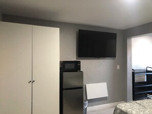 Ein kompaktes Zimmer mit Küchenzeile, einem wandmontierten Flachbildfernseher und einem Bett mit Blumenmusterdecke.
