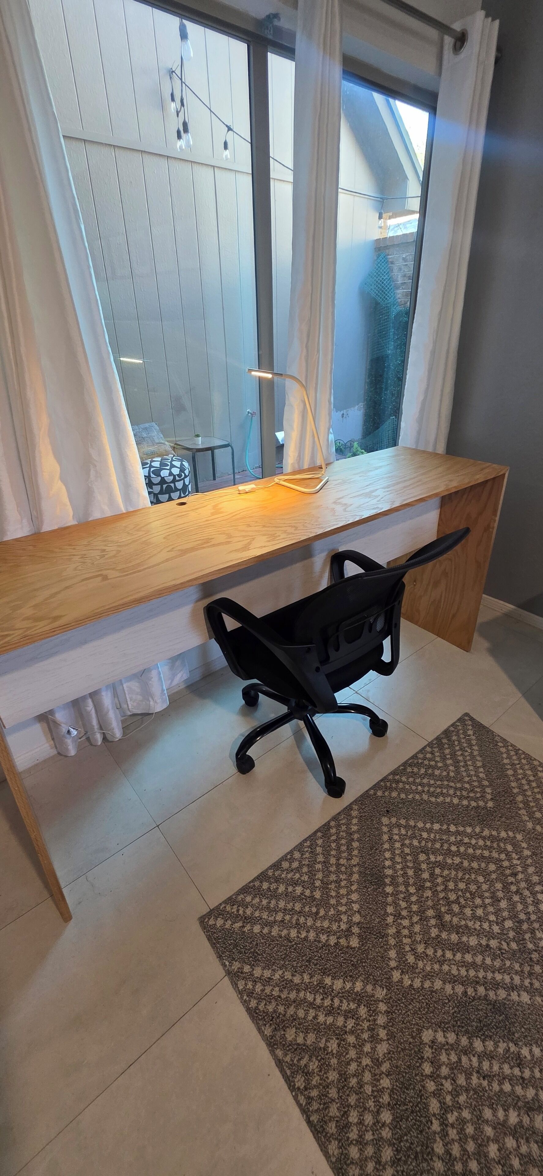 A modern office space with a wooden desk, black office chair, and a patterned rug.