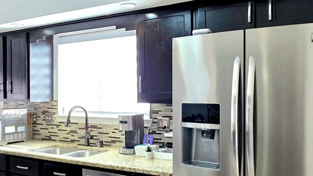 A modern kitchen with stainless steel appliances, a built-in water dispenser, and a large window providing natural light.