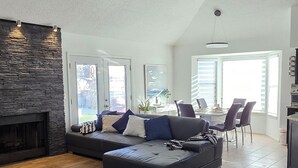 A spacious living room with a fireplace, a ceiling fan, and a dining area with a table and chairs.