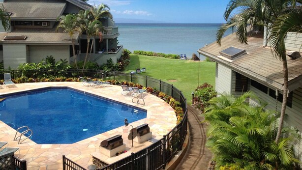 A swimming pool with lounge chairs, a view of the ocean, and a well-maintained lawn. - KAHANA SPACIOUS 3 BEDROOM CONDO; BEACH ON SITE; EXCELLENT VIEWS (Lahaina)