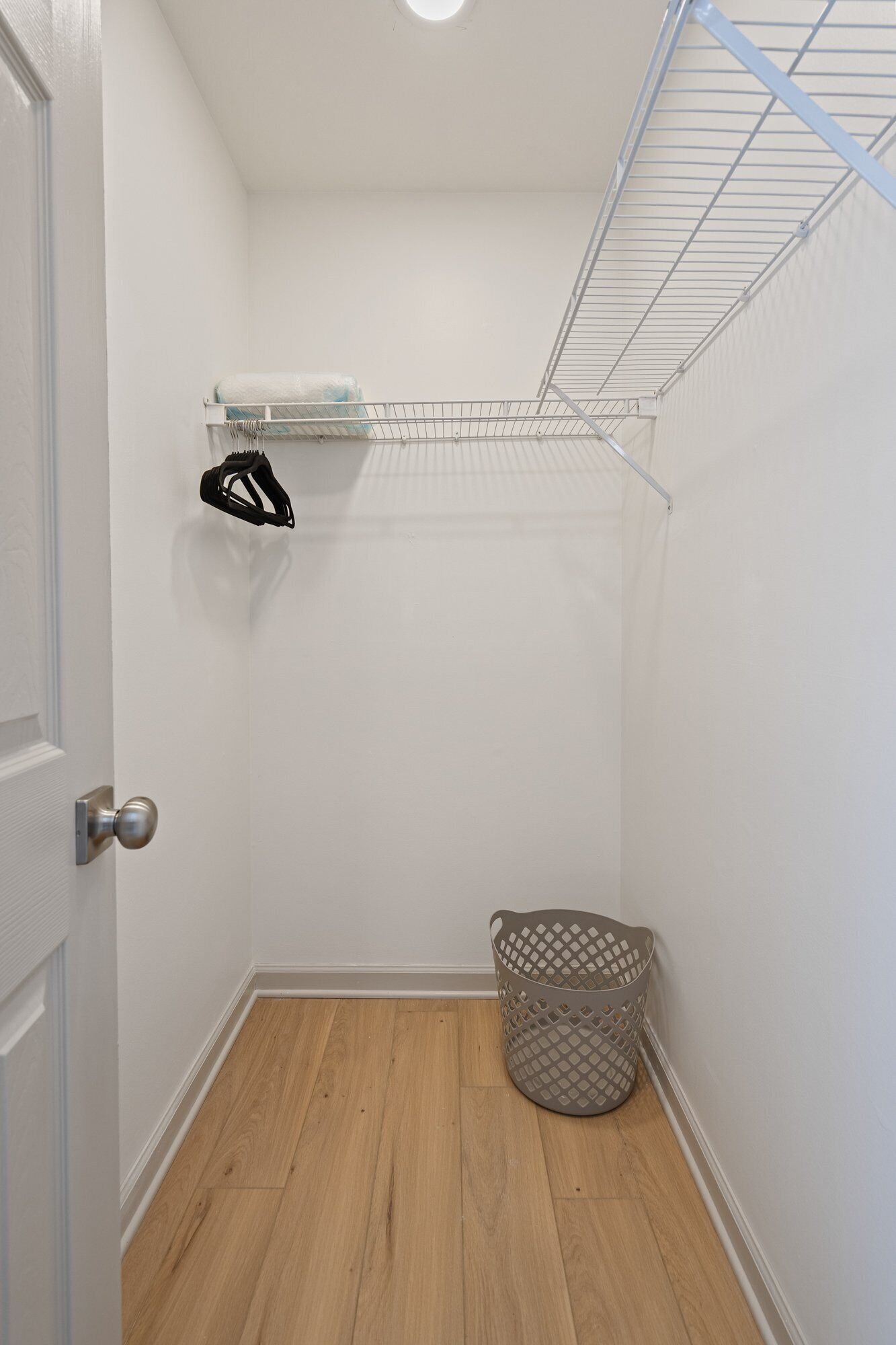 A small, clean laundry room with a metal drying rack, a basket, and a door.