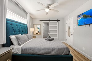 Een slaapkamer met een bed, een plafondventilator, een televisie en uitzicht op zee.