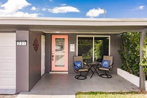 Een gebouw met een garagepoort met het nummer '231', een roze deur en een terras met twee stoelen en een tafel.