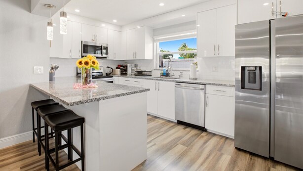 A modern kitchen with white cabinets, stainless steel appliances, and a central island with bar stools. - 🌴 Tropical 3BR Retreat | Huge Screened Patio | Private Yard  | Beaches & D... (Fort Lauderdale)