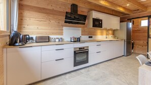 A modern kitchen with wooden ceiling beams, white cabinetry, a built-in oven, and a stainless steel refrigerator.