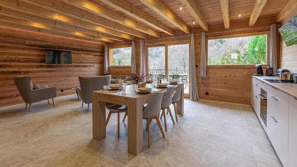 A wooden interior with a dining area, kitchen, and large windows.