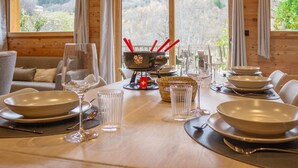 A dining table set for four with clear glasses, plates, and cutlery. A decorative bowl with red handles is centered on the table.