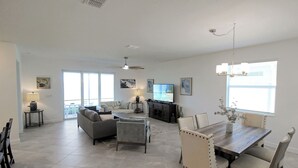Un ampio soggiorno con un divano grigio, un tavolo da pranzo in legno con sedie, una televisione e una ventola a soffitto.